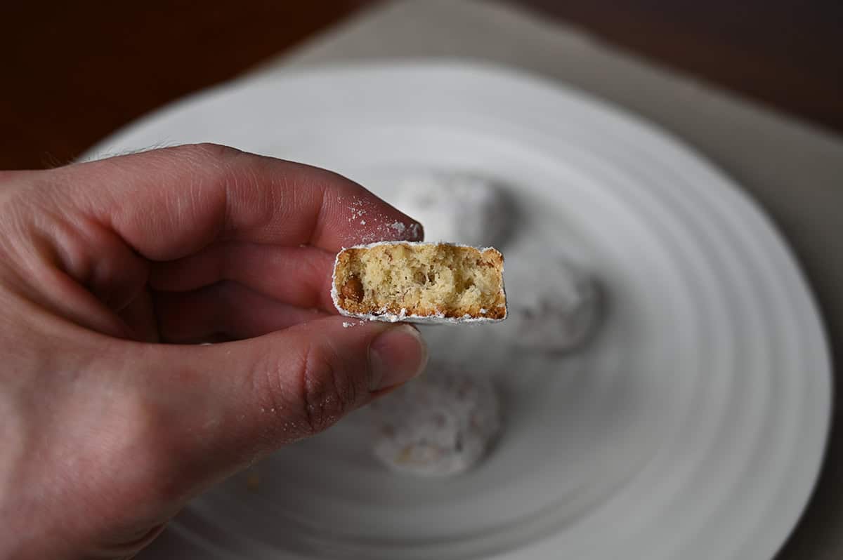 Image of a hand holding one pecan meltaway with a bite taken out of it close to the camera so you can see the inside.