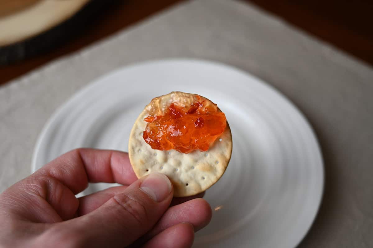 Image of a hand holding one cracker close to the camera with red chili pepper spread on the cracker.