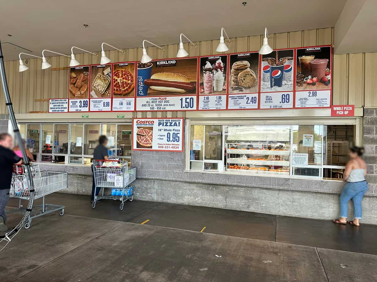 Image of the Costco Hawaii food court menu signage with people lined up and  waiting for their food. 