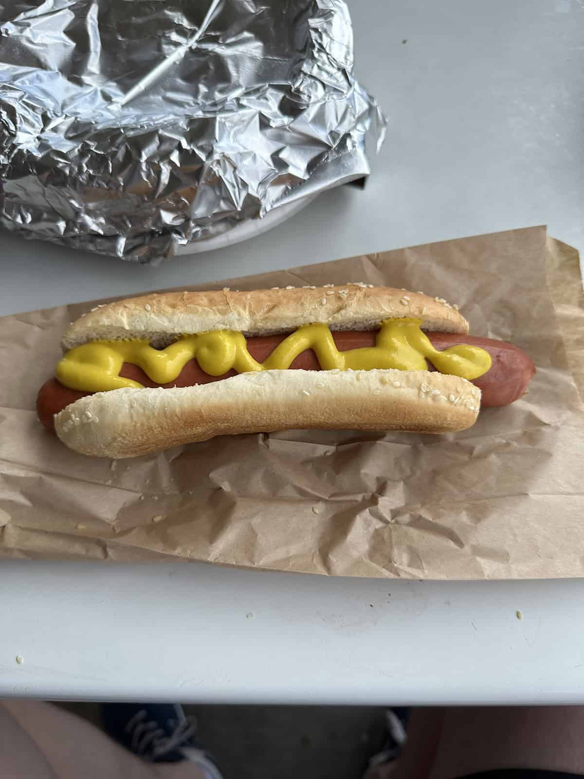 Top down image of a Costco food court hot dog sitting on a paper bag with mustard on it.