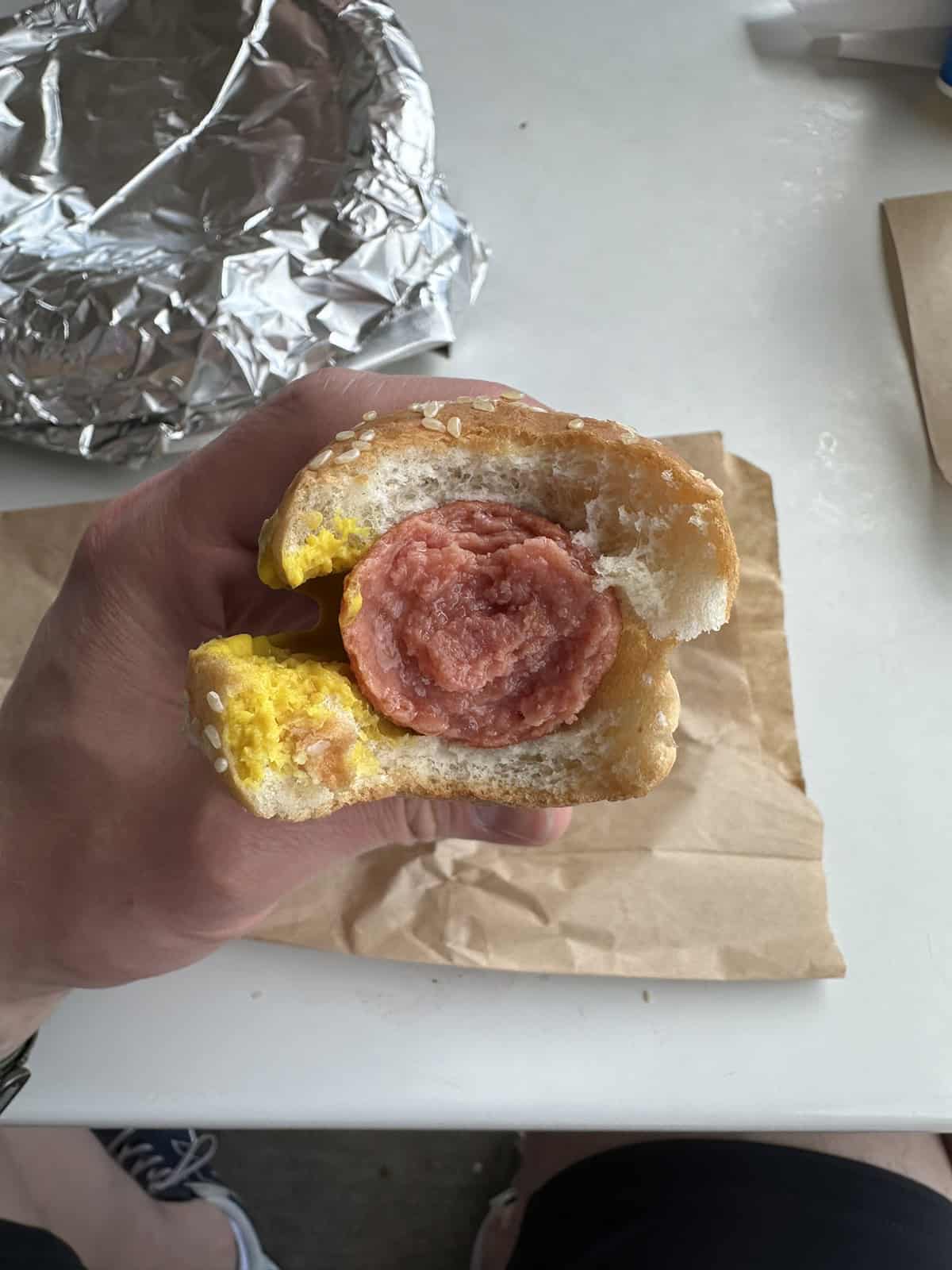 Image of a hand holding a Costco food court hot dog with a few bites taken out of it so you can see the center of the sausage.