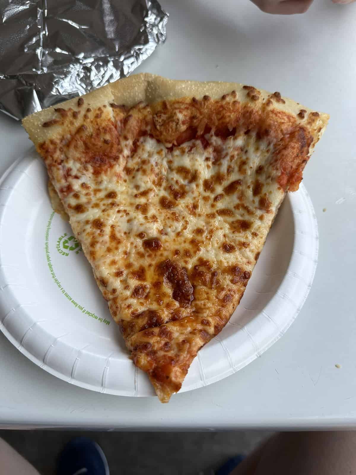 Top down image of one large slice of Costco food court cheese pizza served on a paper plate.