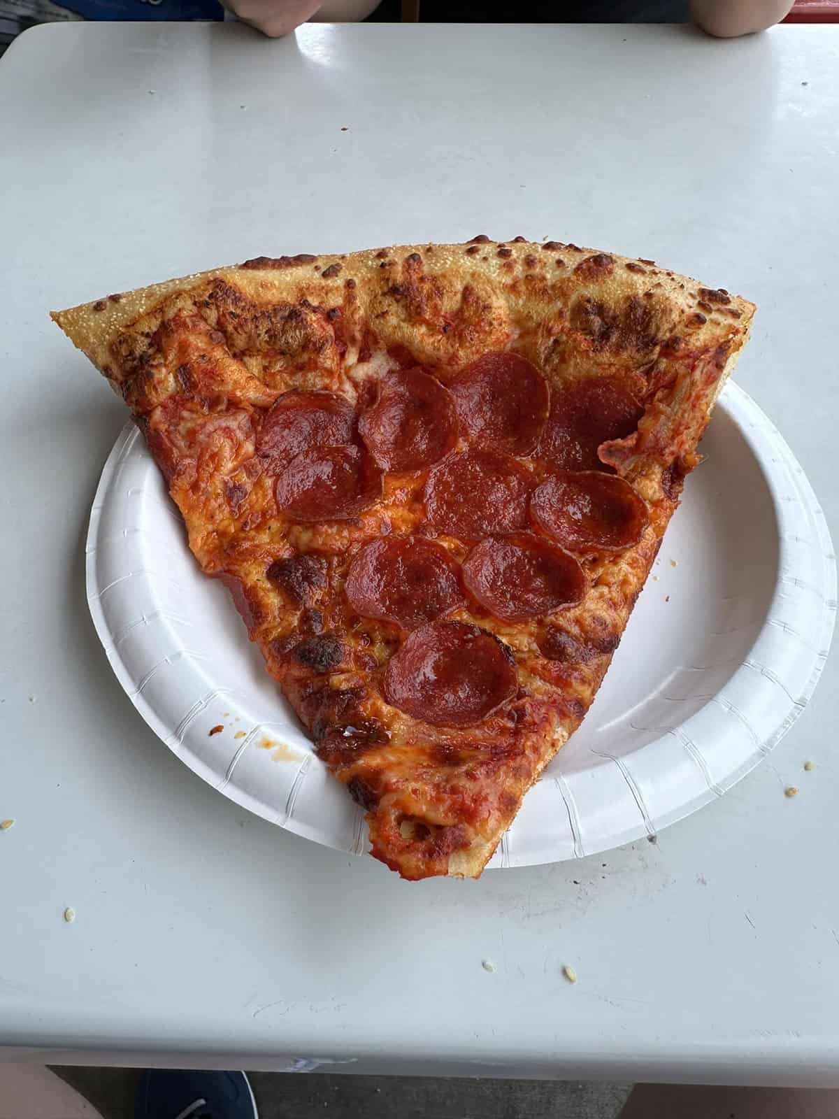 Top down image of one large slice of Costco food court pepperoni pizza served on a paper plate.