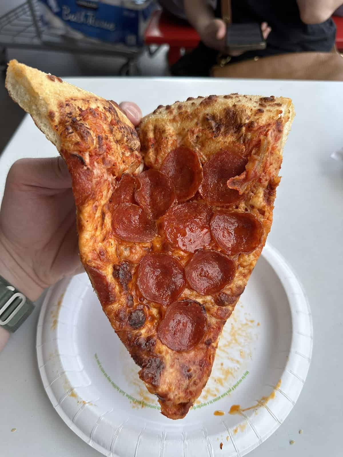 Closeup image of a hand holding one slice of pepperoni pizza close to the camera, the pizza slice is slightly folded in half. 