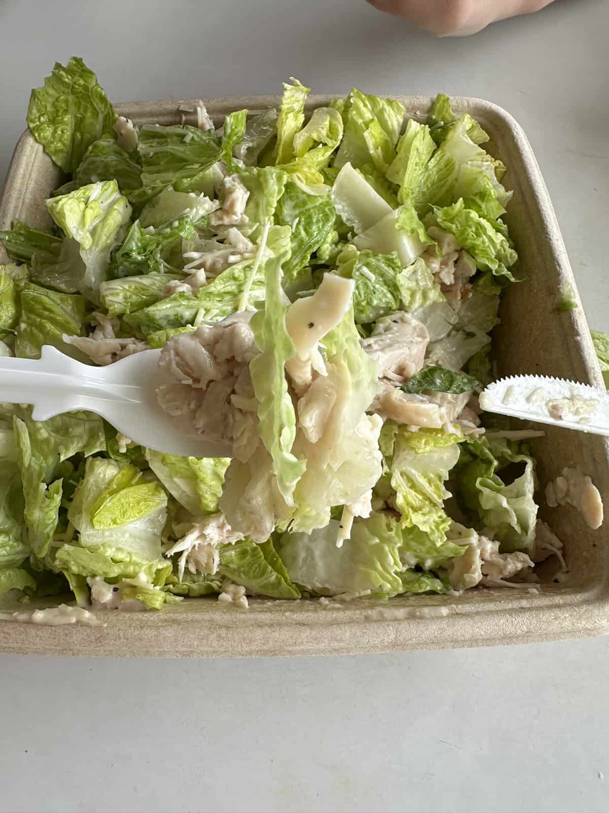 Top down closeup image of the chicken Caesar salad from the Costco food court. There is a fork with a bite of salad on it close to the camera, hovering over the salad.