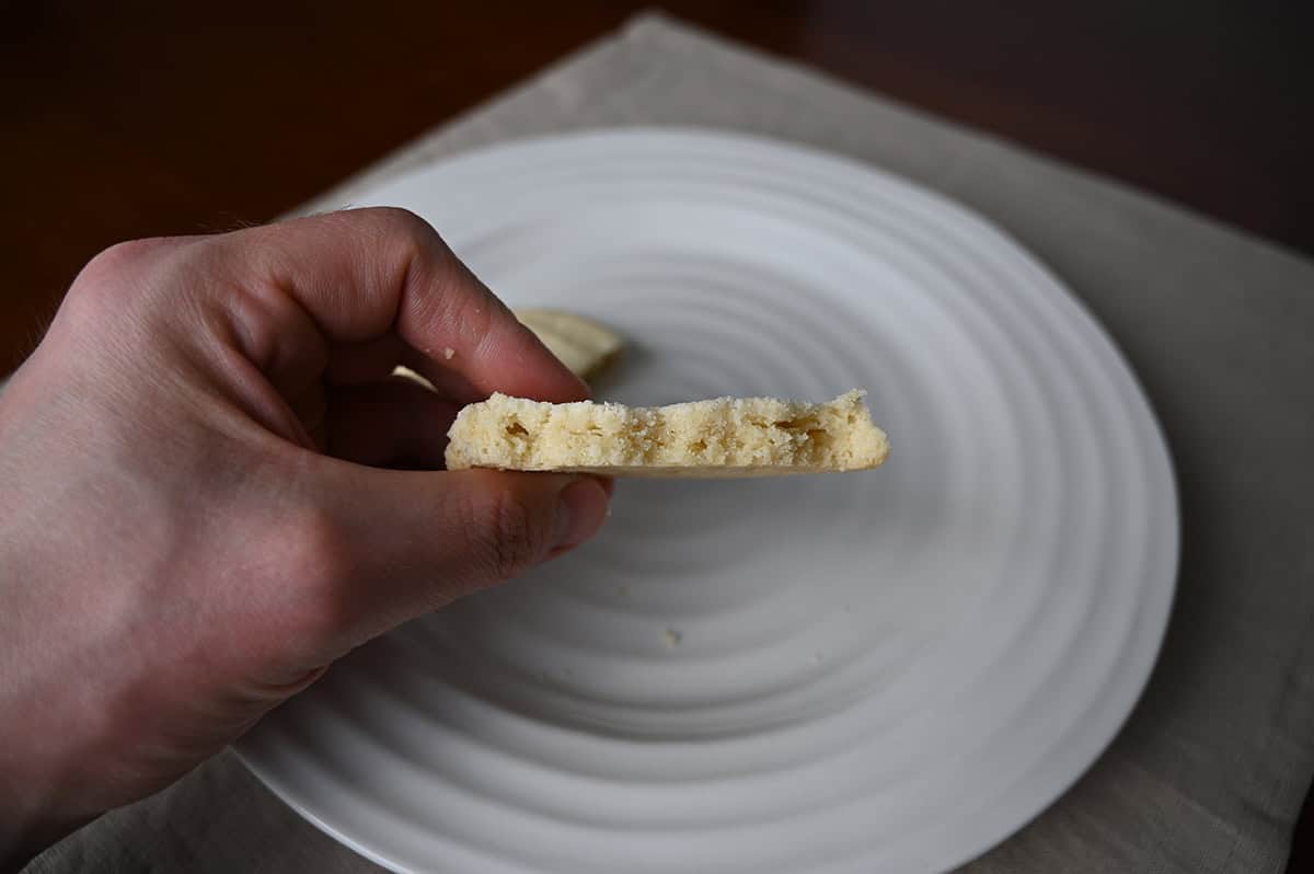 Image of a hand holding one Costco Kirkland Signature Butter Shortbead Cookie on it's side with a few bites taken out of it so you can see the center of the cookie.