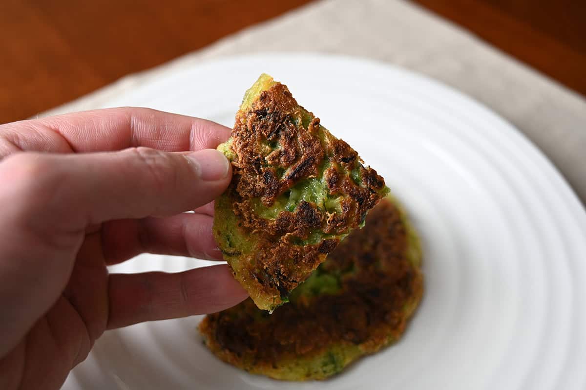 Closeup image of a hand holding one piece of cooked vegetable pancake close to the camera. 