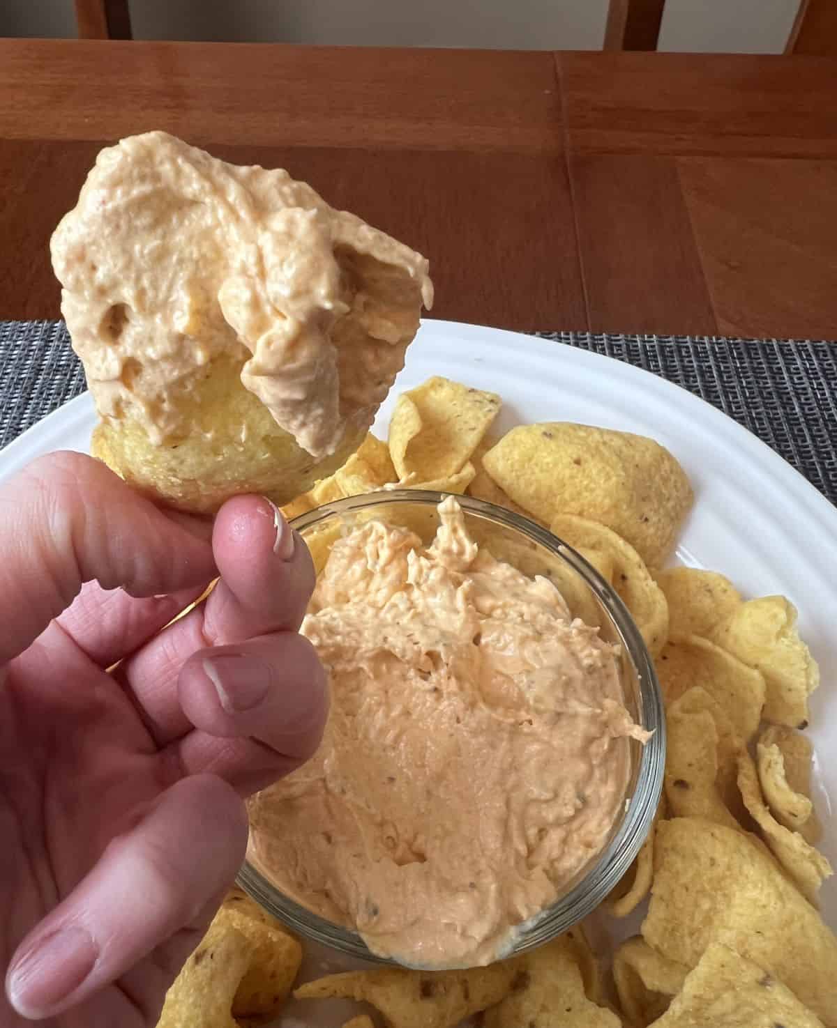 Image of a hand holding one tortilla chip with dip on it close to the camera.