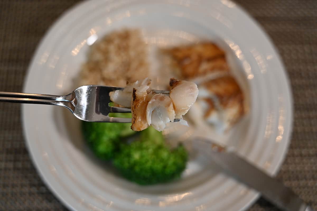 Closeup image of a forkful of cod with a plate of cod, brocolli and rice in the background of the image.
