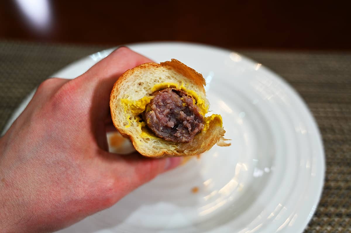 Image of a brat in a bun with mustard on it. There's a bite taken out of the bun and sausage and it's angled towards the camera so you can see the inside of the sausage.