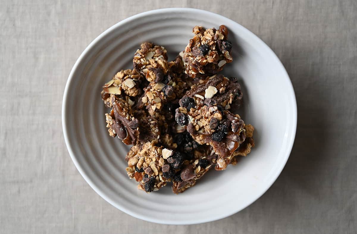 Top down image of a white bowl full of oat based granola clusters with dried blueberries Snappers. 