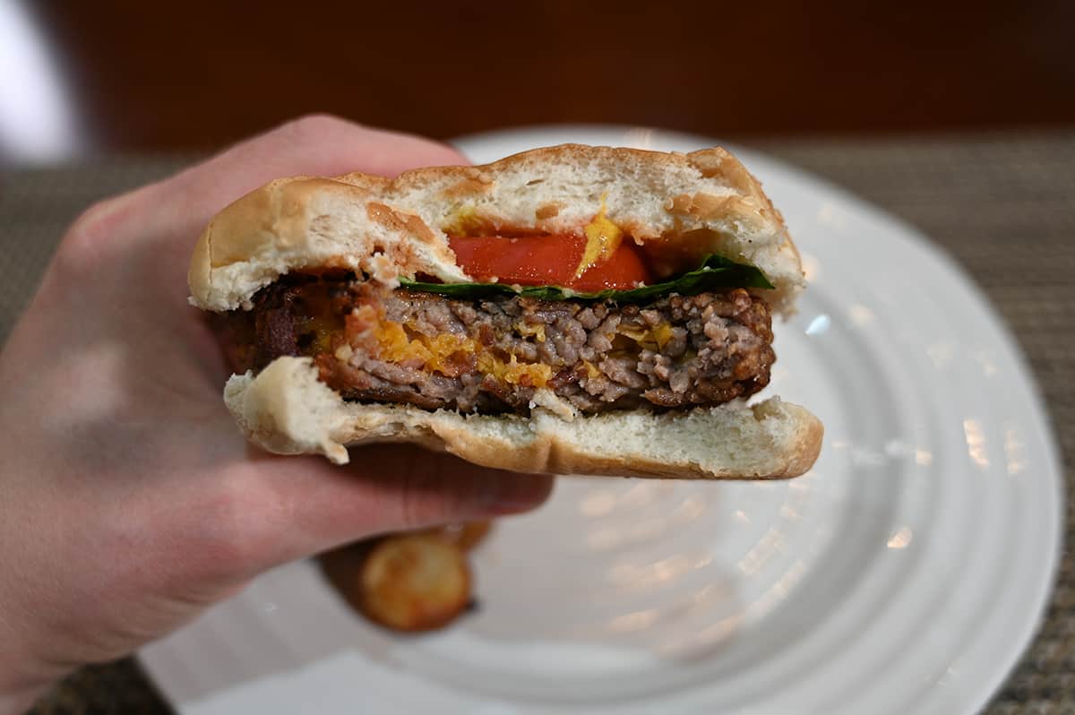 Closeup image of a hand holding a bacon and cheddar stuffed burger with a few bites taken out of it close to the camera.