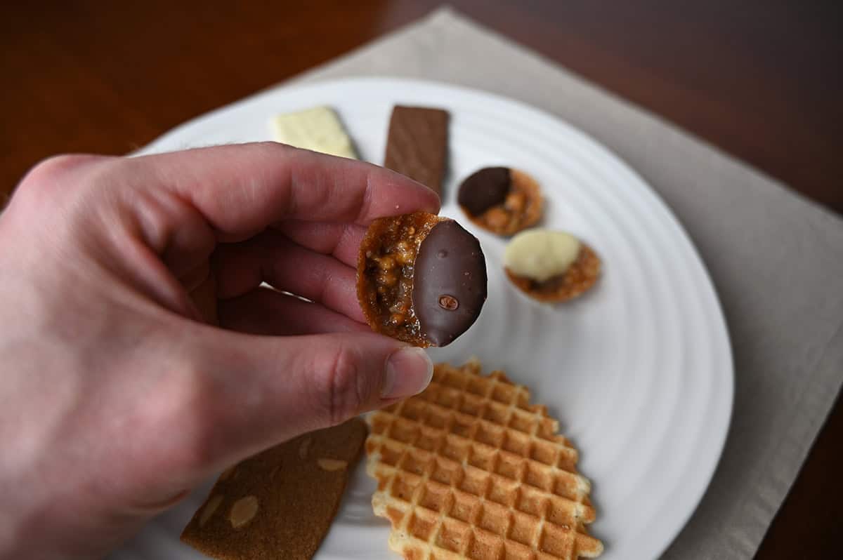 Image of a hand holding one dark chocolate florentine close to the camera.