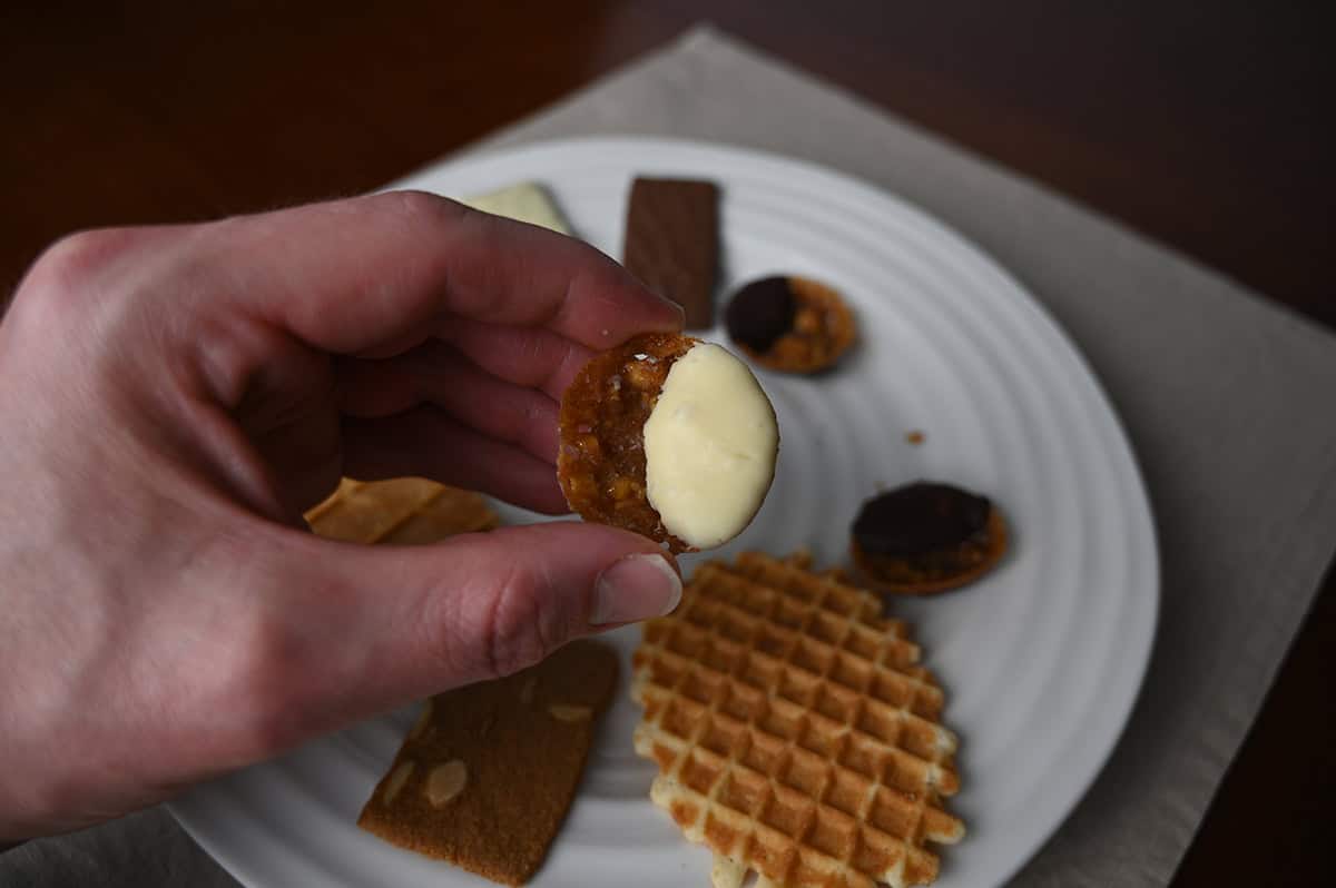 Image of a hand holding one white chocolate almond florentine close to the camera.