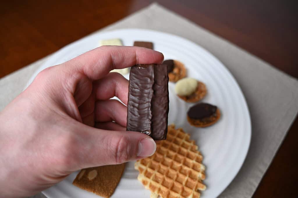 Image of a hand holding one dark chocolate thin close to the camera.