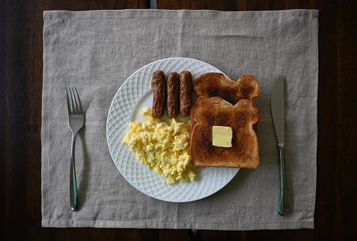 Top down image of a white plate with eggs, three sausages and a piece of toast with a big square of butter on the toast. 