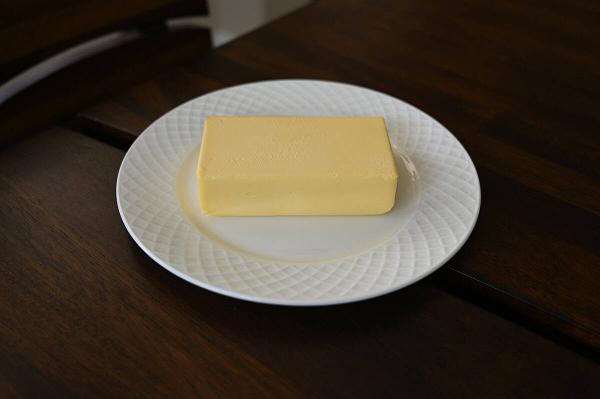 Sideview image of one brick of butter on a white plate.