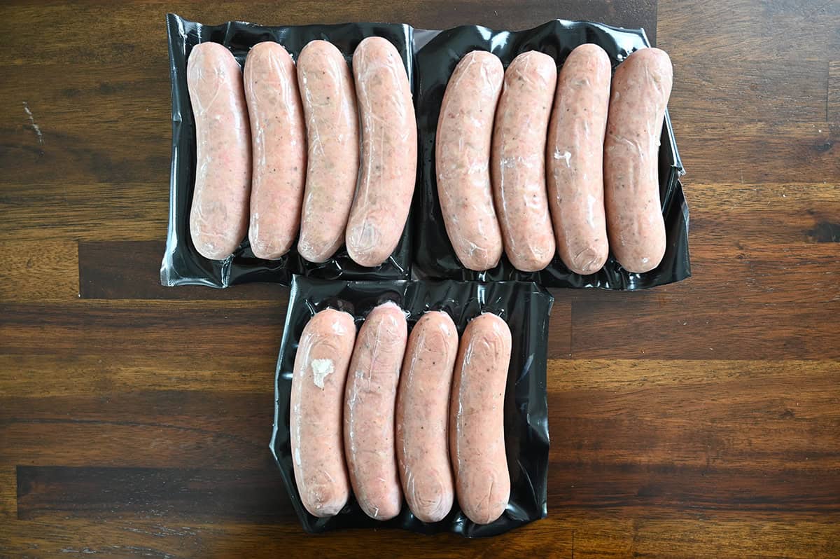 Image of three packs of uncooked sausages sitting on a table unopened. There are four sausages in each pack.