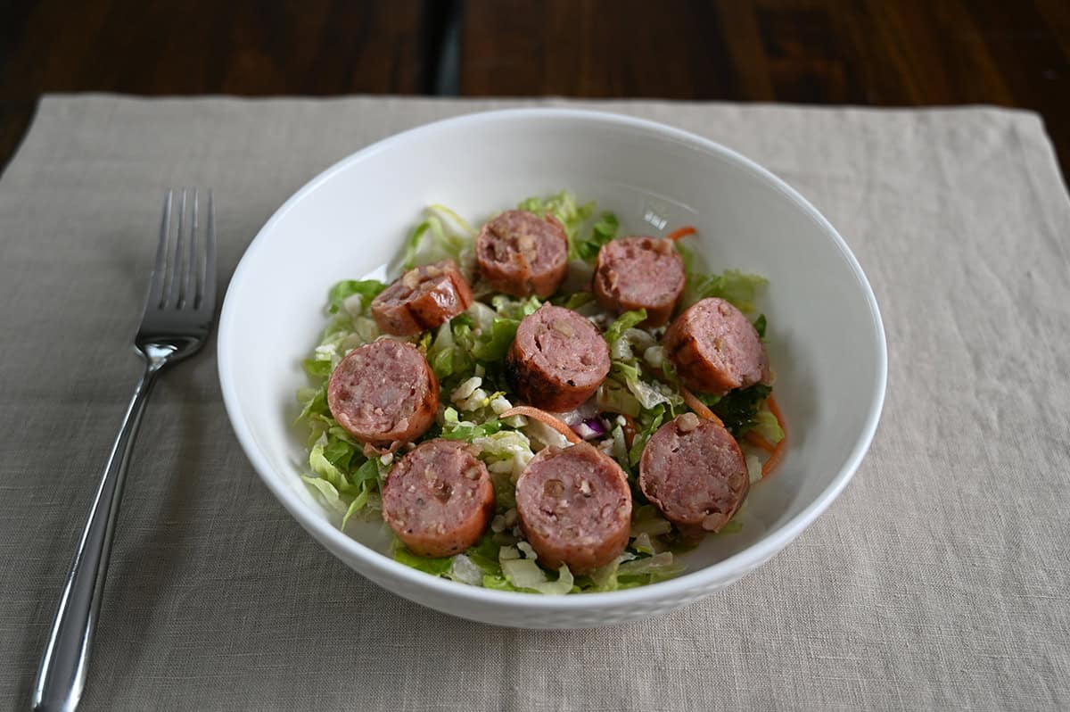 Top down image of a bowl of salad with chicken sausage cut on top.