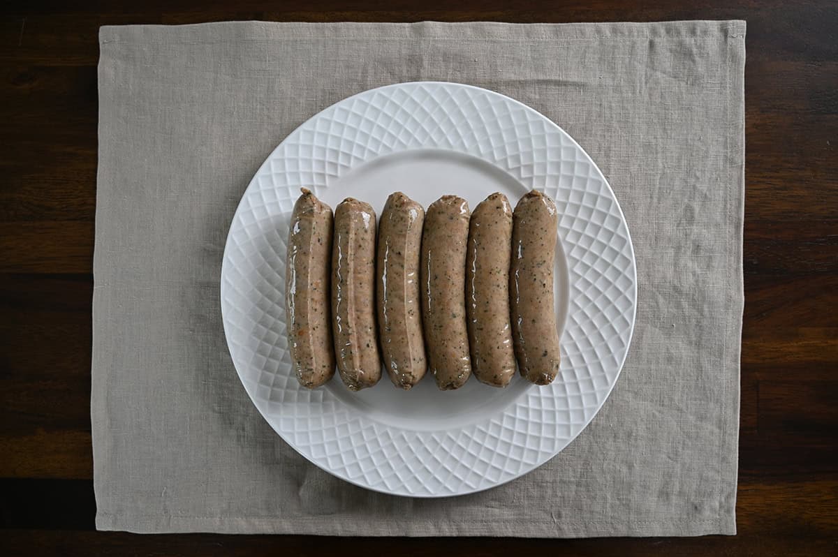 Top down image of six sausages served on a white plate ready uncooked.