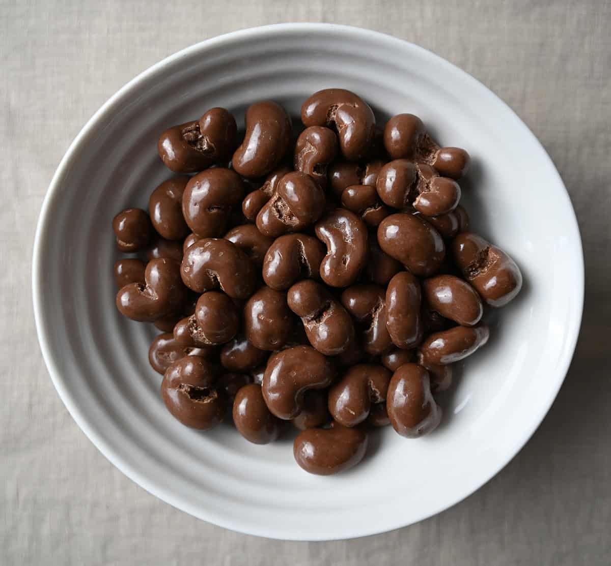Top down image of a white bowl full of chocolate covered cashews. 