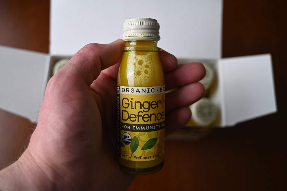 Closeup image of a hand holding one bottle of ginger defence.