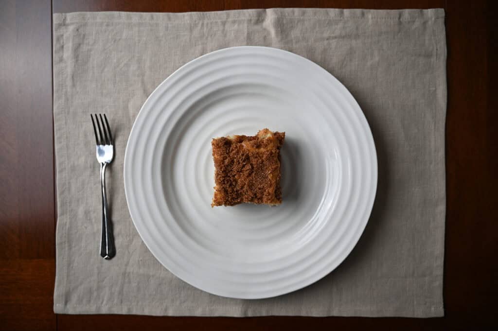 Top down image of one piece of cinnamon swirl cake served on a white plate beside a fork.