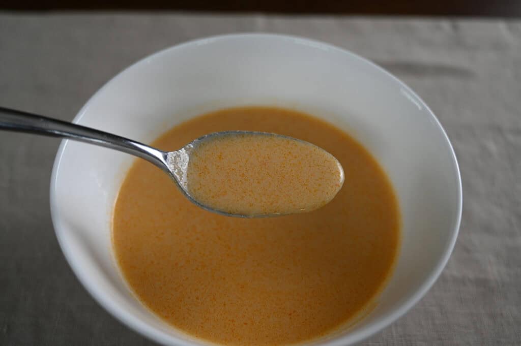 Closeup image of a spoon with soup on it hovering over a bowl of lobster bisque.