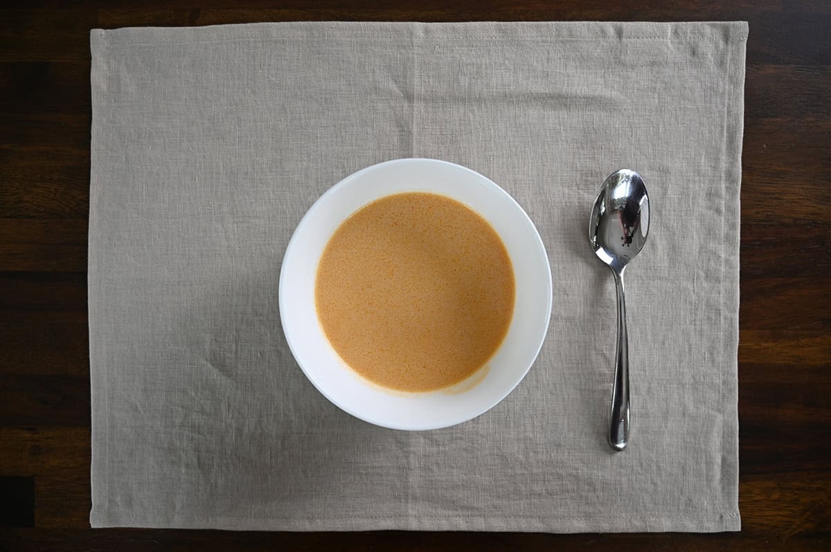 Top down image of a bowl of lobster bisque served on a placemat beside a spoon.