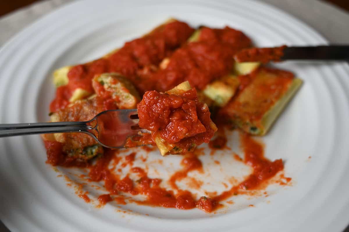 Closeup image of a fork holding a small bite of cannelloni covered in marinara sauce.