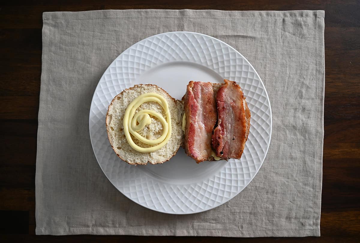 Top down image of an open-faced sandwich with pork belly on one side of the bun and mayo on the other side of the bun.