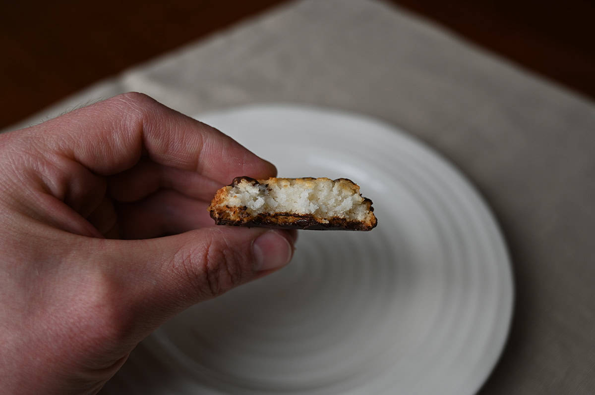 Side view image of a hand holding a cookie with a bite taken out of it so you can see the coconut center.