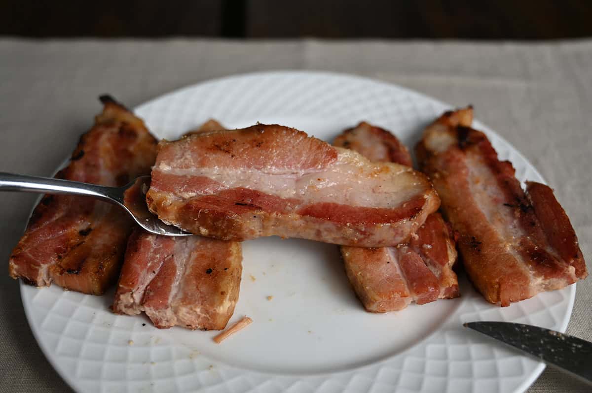 Side view image of a fork with one slice of pork belly resting on top of the fork.