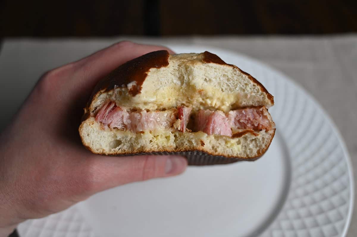 Side view image of a hand holding a pork belly sandwich with a few bites taken out of it so you can see the pork belly. 