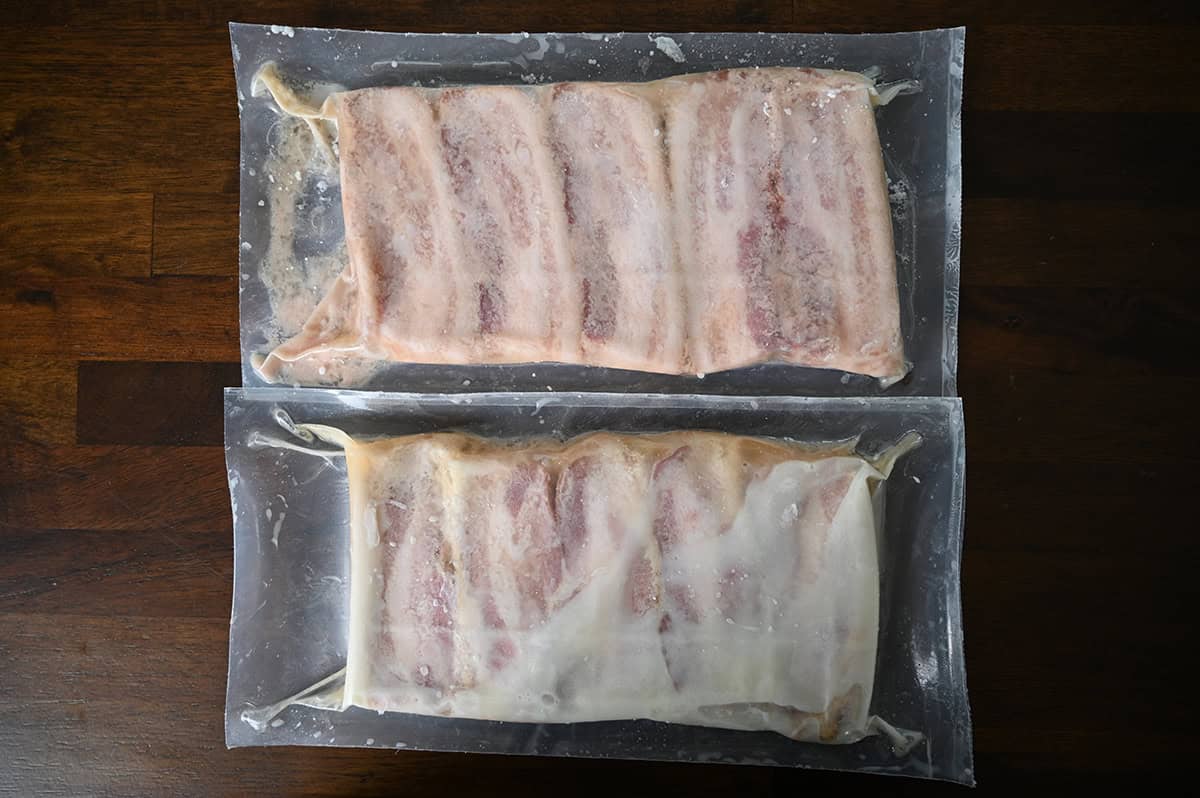Top down image of two unopened uncooked packages of pork belly sitting on a table.