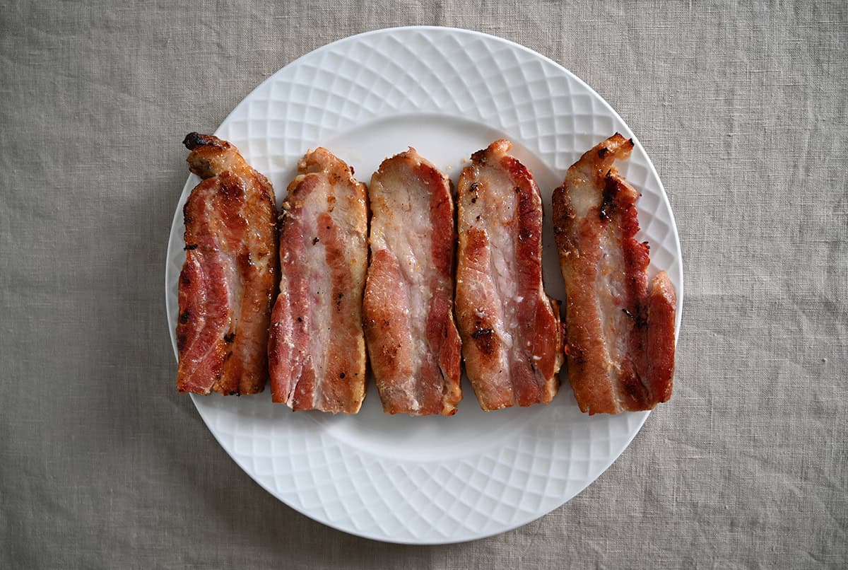 Top down image of five slices of pork belly cooked and served on a white plate.