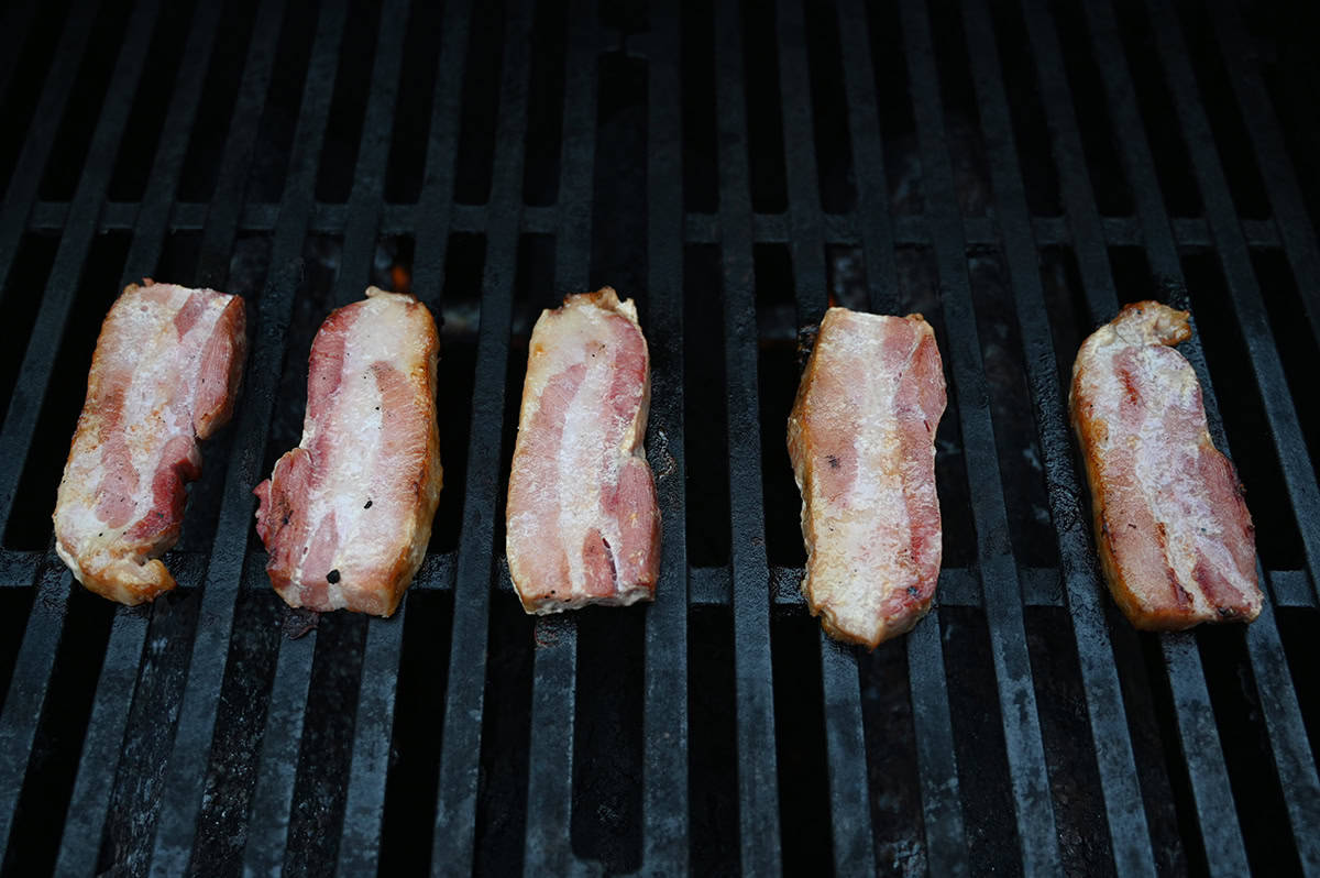 Top down image of five pieces of pork belly being grilled on a barbecue.