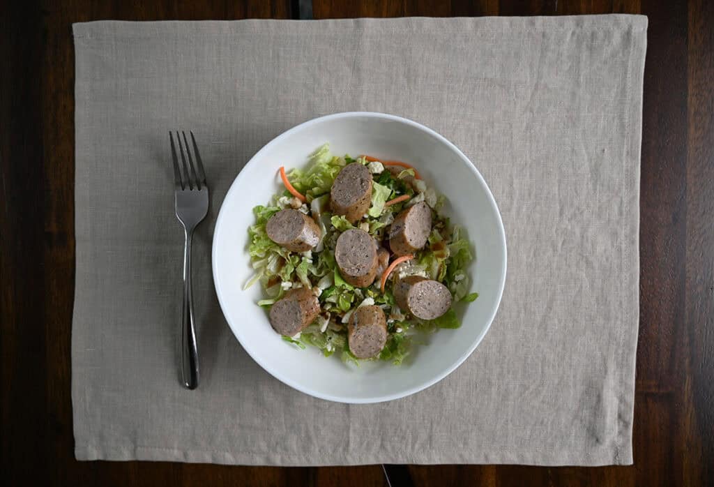 Top down image of a bowl of salad with sausage slices served on top.