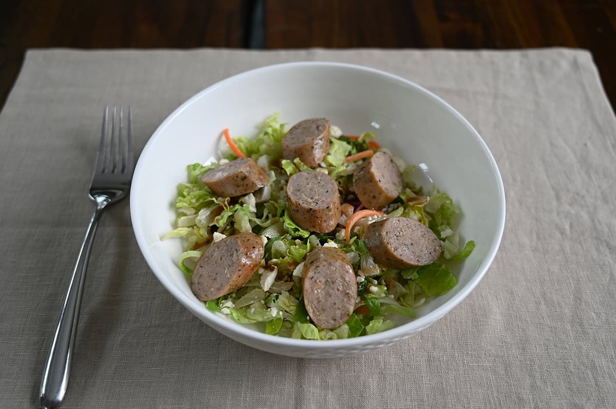 Closeup image of a bowl of salad with sausage slices served on top.