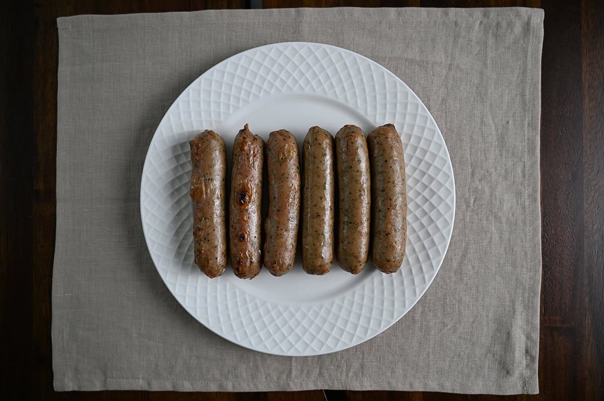 Top down image of six cooked sausages served on a white plate.