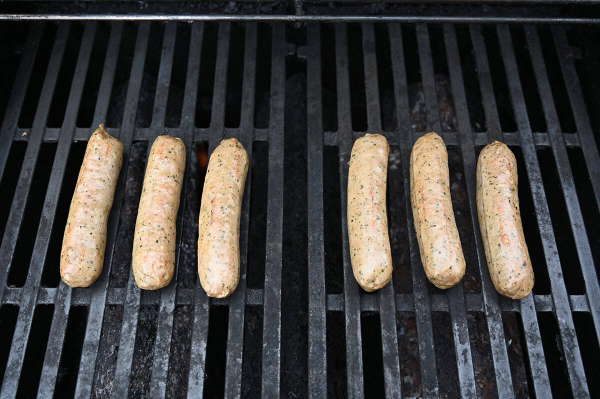 Top down image of six sausages being cooked on a barbecue grill.