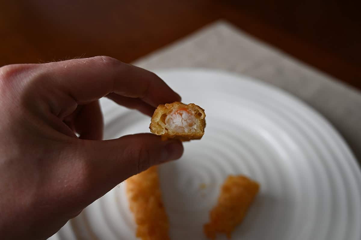 Sideview image of a hand holding one tempura shrimp close to the camera with a few bites taken out so you can see what the shrimp look like.