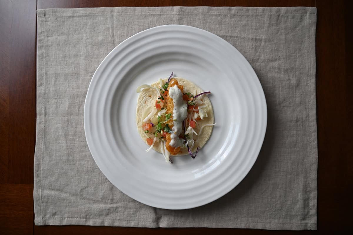 Top down image of a tortilla served on a white plate. In the middle of the tortilla is shrimp, slaw, salsa and sauce.