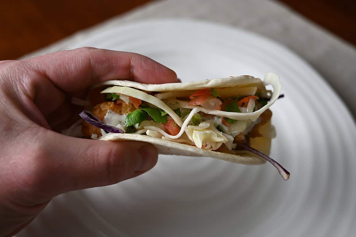 Sideview image of a hand holding one taco close to the camera with a few bites taken out of it so you can see the filling.
