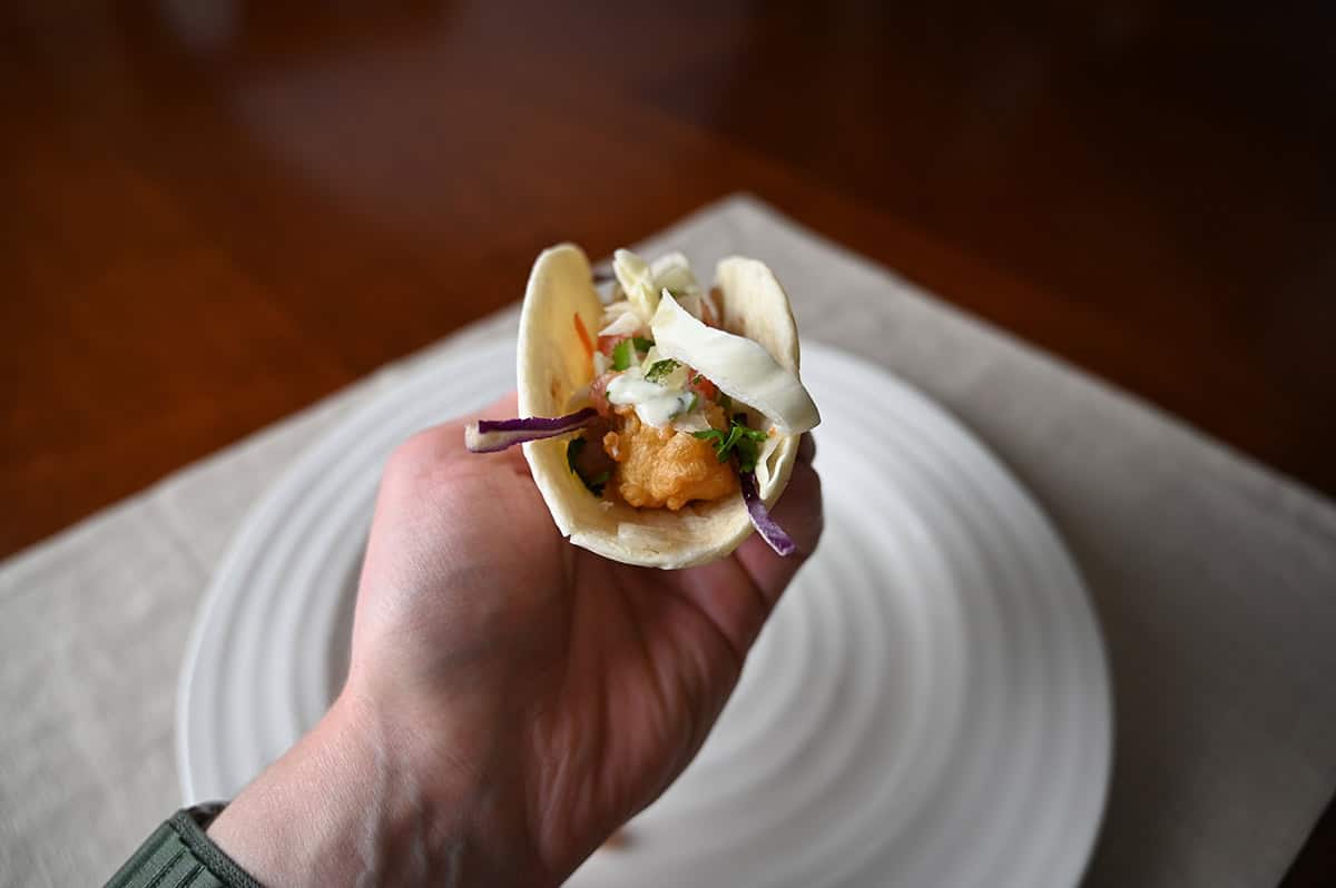 Sideview image of a hand holding one taco close to the camera so you can see one shrimp in the taco with slaw on top.