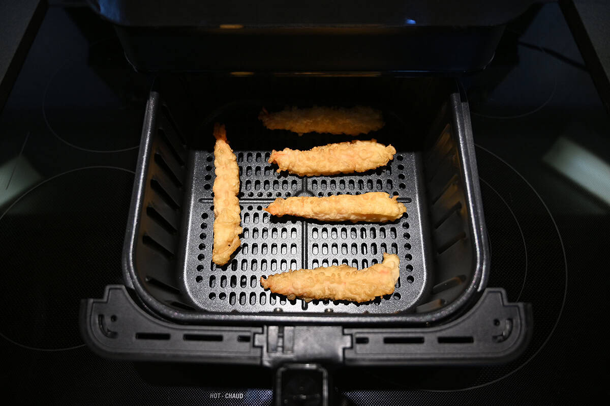 Top down image of four shrimp tempura sitting in an air fryer before being cooked.