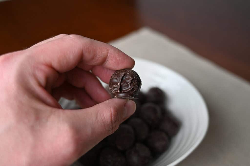 Closeup image of a hand holding one truffle close to the camera with a bowl of truffles in the background.