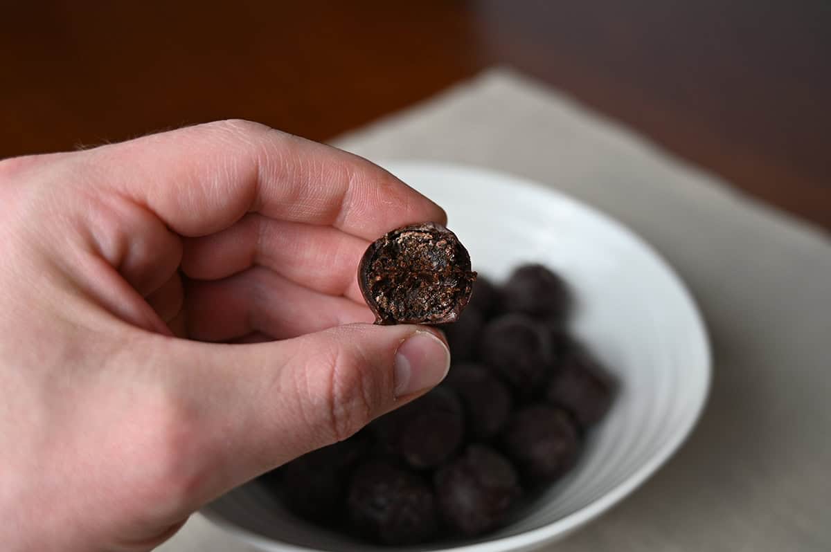 Closeup image of a hand holding on truffle with a bite taken out of it so you can see the fig center.