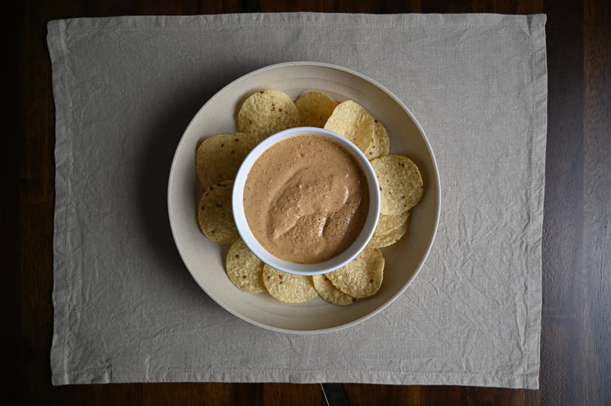 Top down image of a plate of tortilla chips served with a bowl of sauce in the middle.