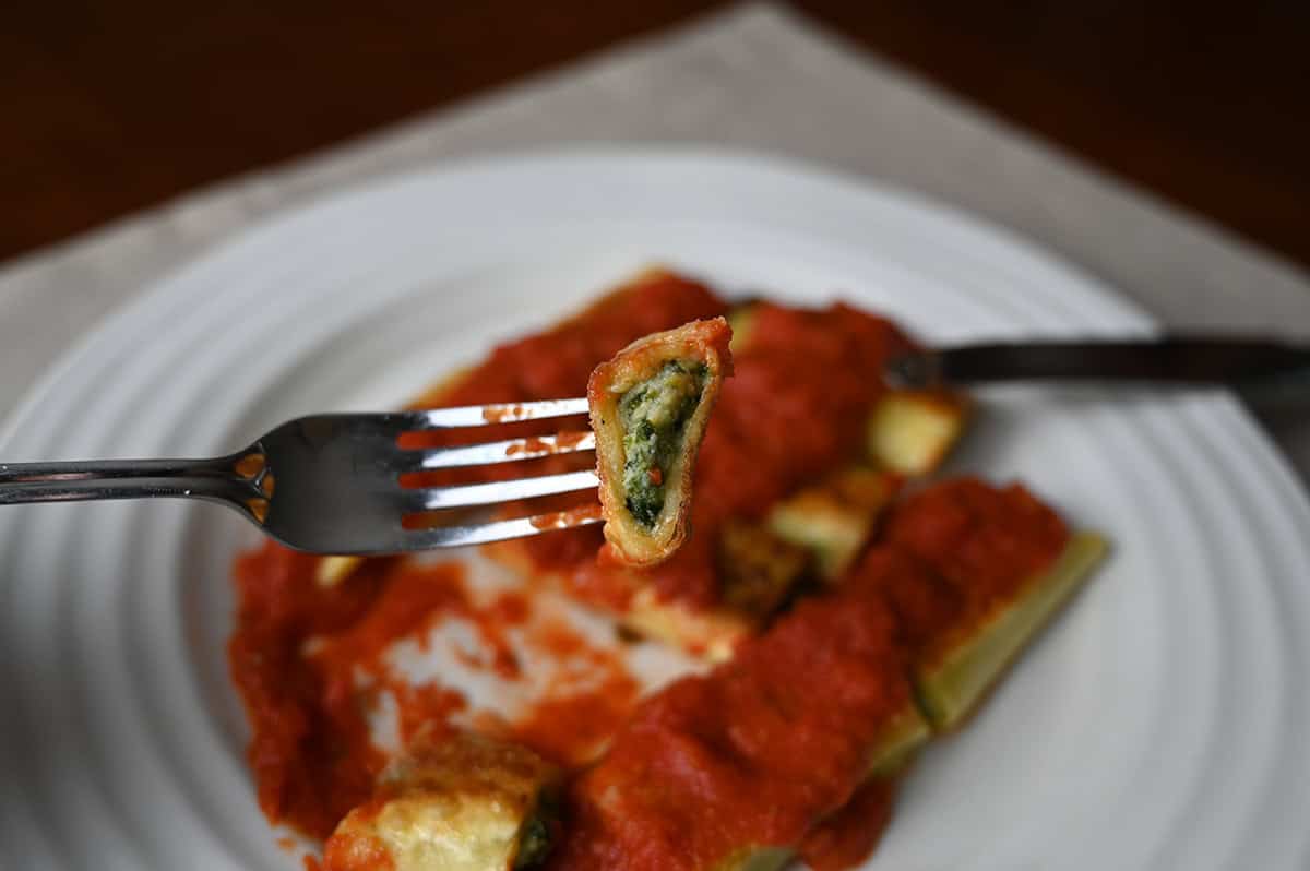 Closeup image of a fork with a bite of cannelloni on it close to the camera so you can see what the inside looks like. 